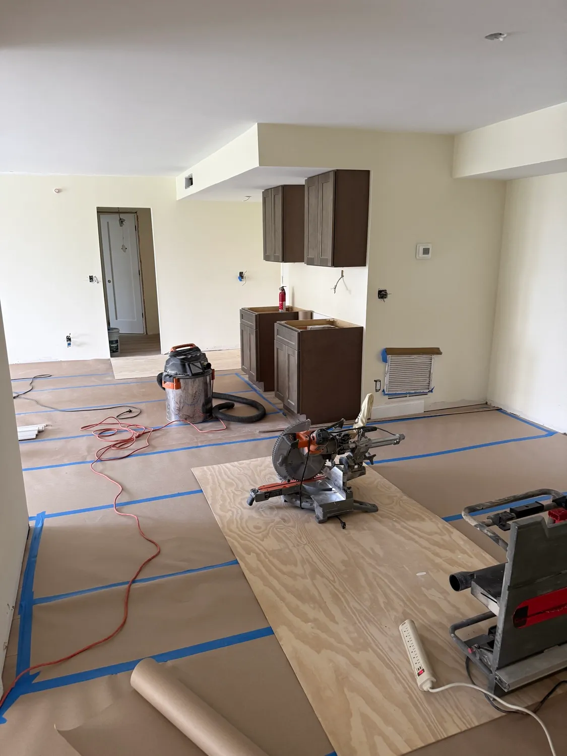 Dark wood cabinets going in with the floors covered in protective paper and a miter saw set up