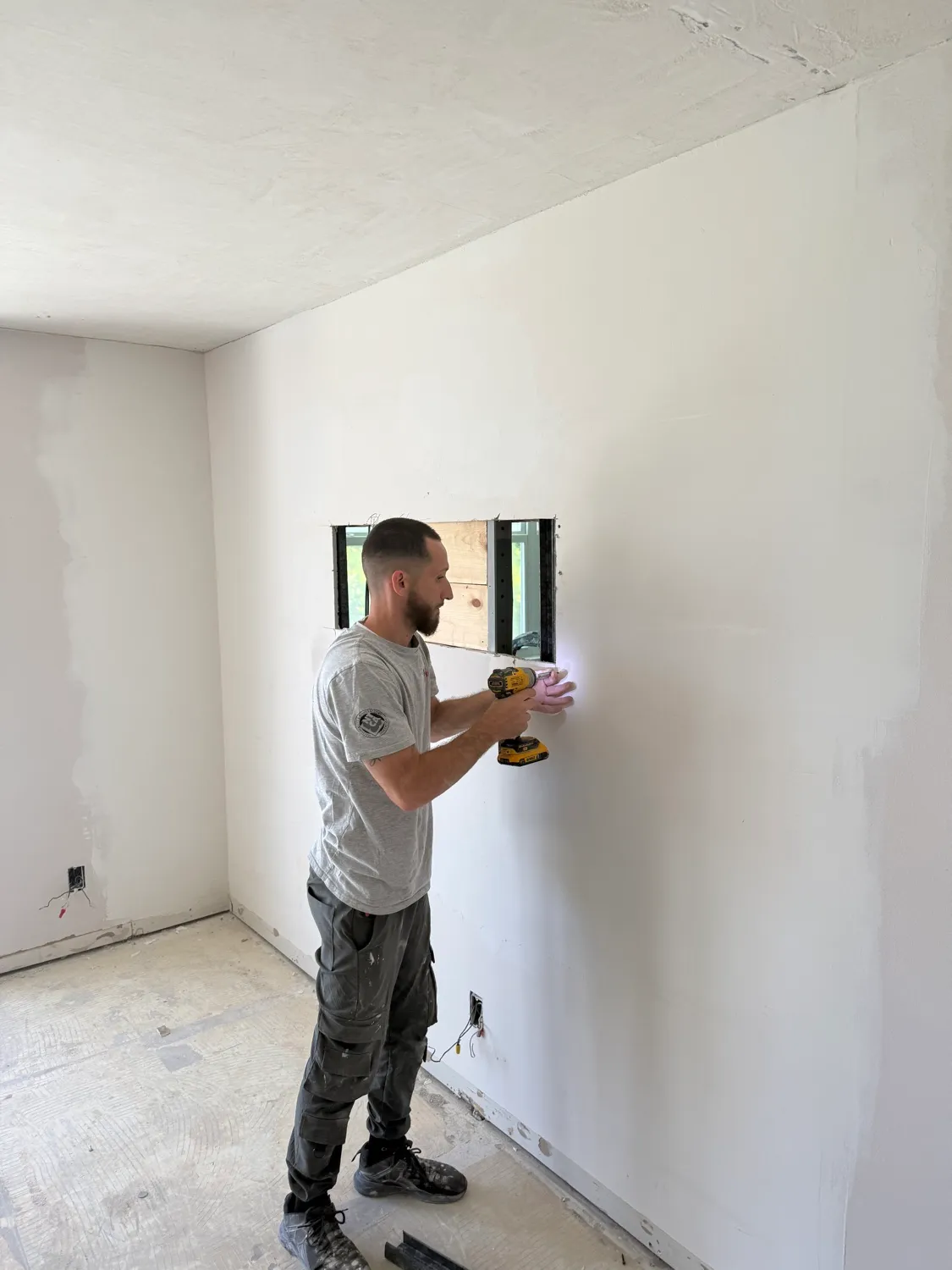 Worker fastening drywall around an opening in a freshly skimmed bedroom wall