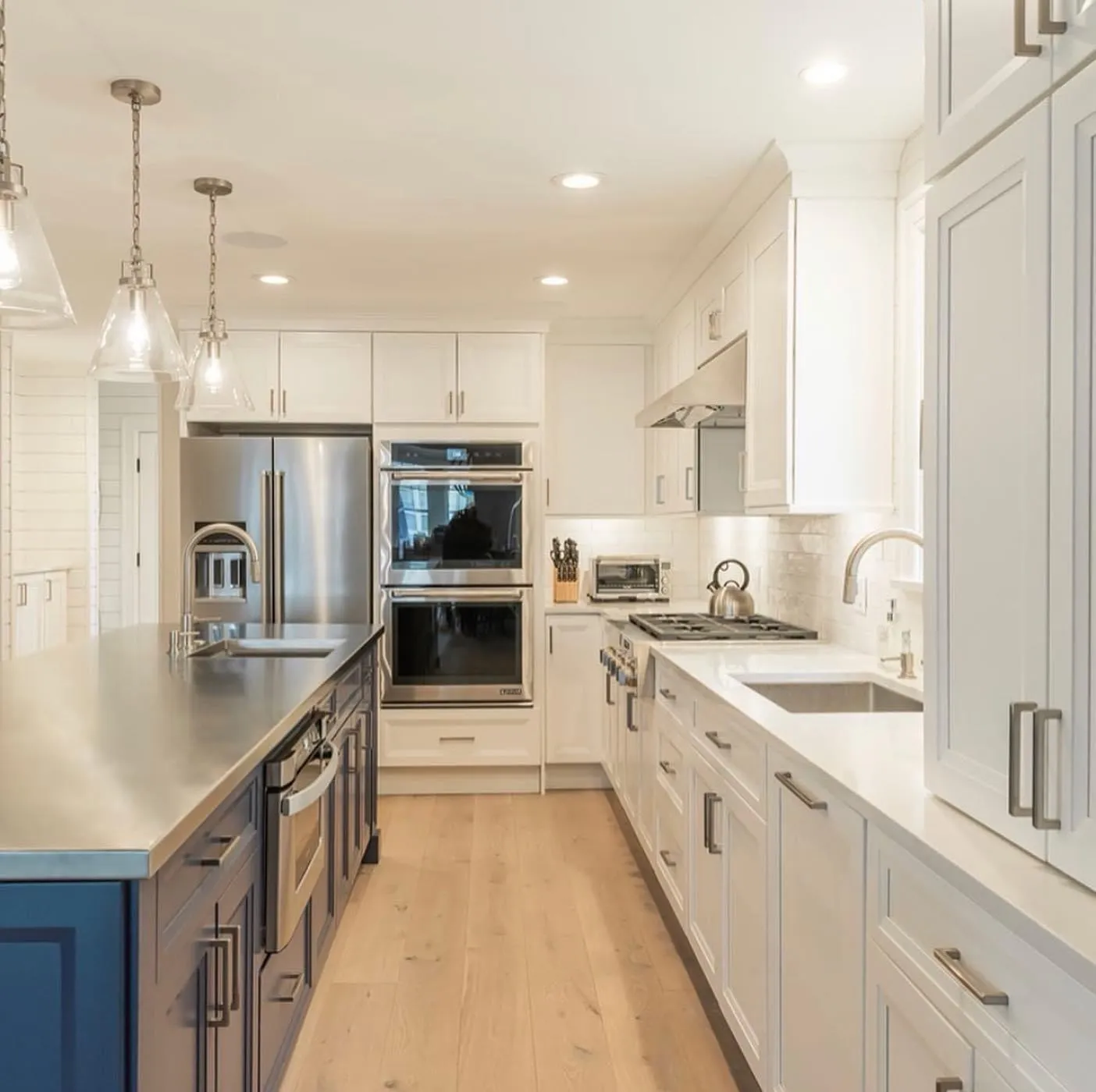 White kitchen with a navy island, stainless double ovens, and pendant lights