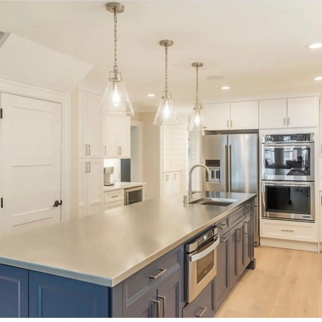 Kitchen island with a navy base, built-in wall ovens, and glass pendants