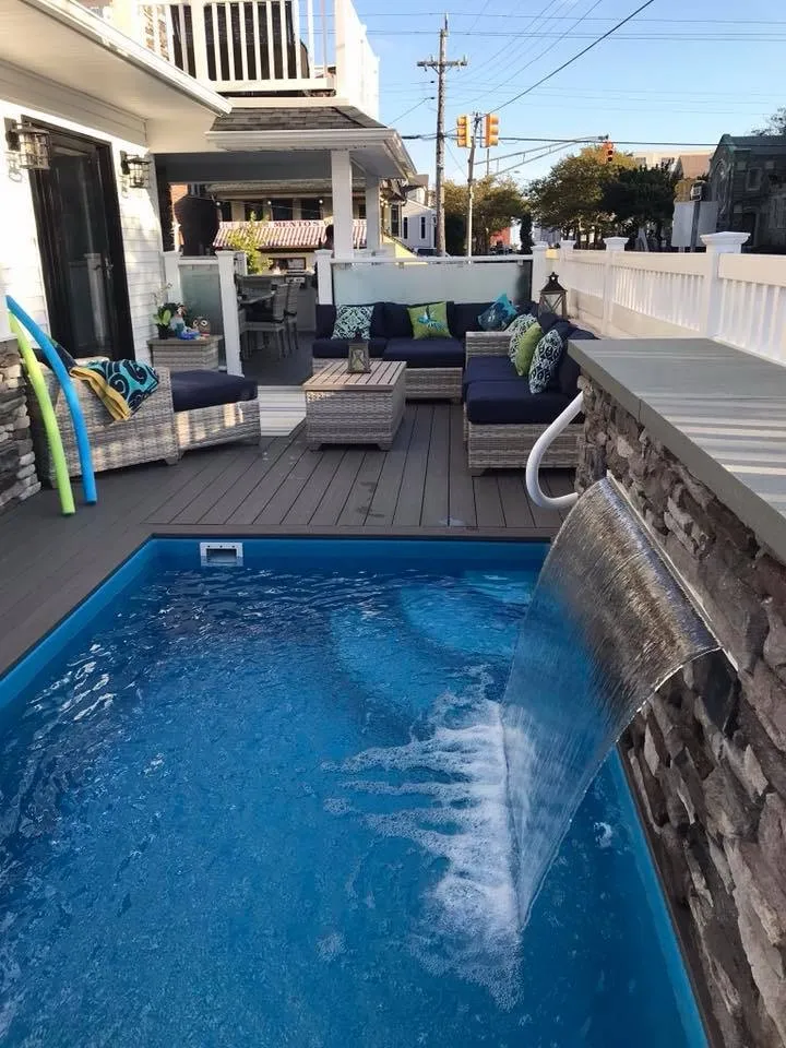 Backyard plunge pool with a water feature beside a covered lounge deck