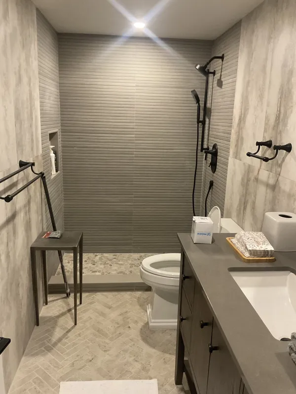 Walk-in shower with textured tile, black fixtures, and a wood vanity