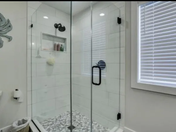 Frameless glass shower with a pebble floor and white tile walls