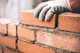 Gloved hand setting a red brick into fresh mortar during masonry work